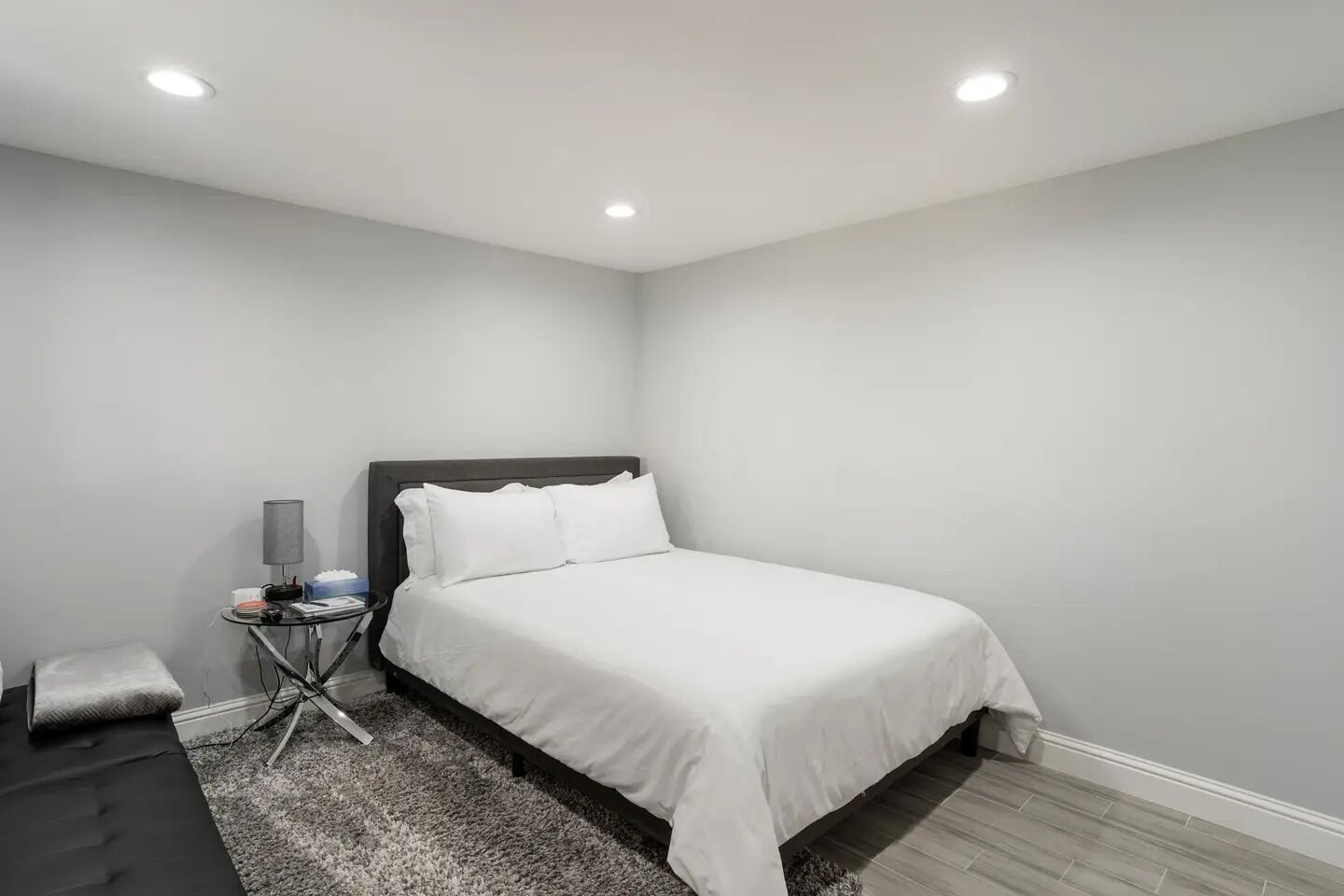 A modern bedroom with a single bed, a bedside table, a lamp, and a small rug.