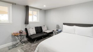 A modern hotel room with a large bed, a black leather sofa, a small side table, and a window with curtains. - Private Pacifica suite near the beach (Pacifica)