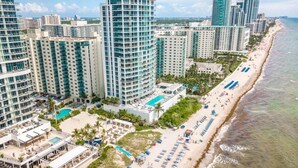 Ein Hotel an der Küste mit mehreren Hochhäusern, einem Strand mit Liegestühlen und einem Poolbereich.