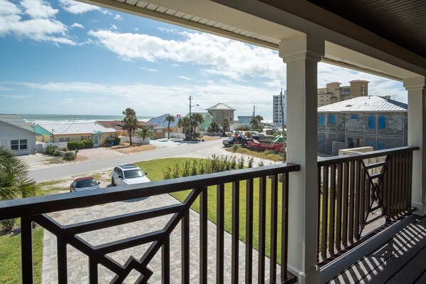 A residential area with a paved driveway, parked cars, and a view of the ocean.