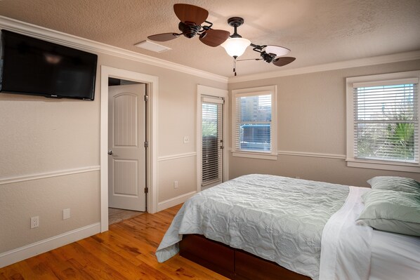 A bedroom with a bed, a ceiling fan, a TV mounted on the wall, and a window with blinds.