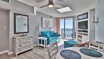 A modern living room with a blue sofa, a white dining table, and a ceiling fan.