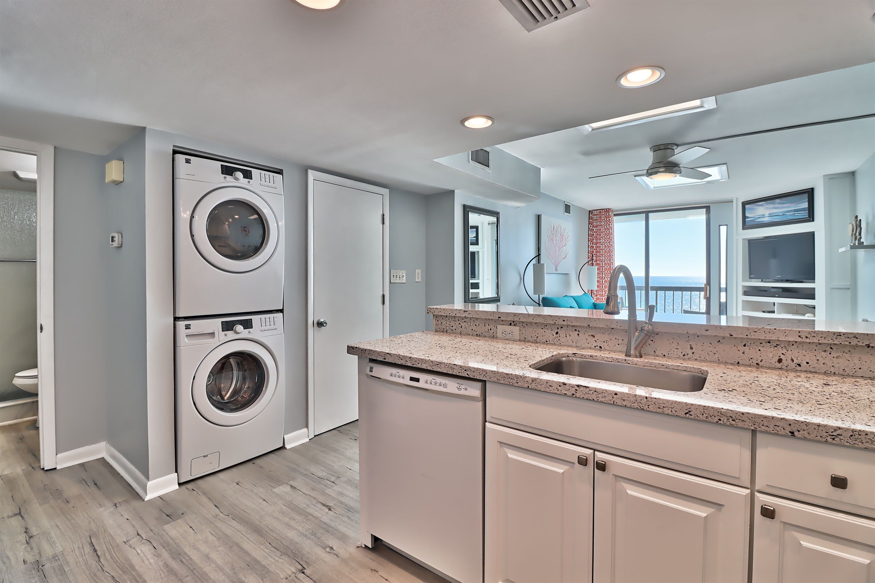 A modern kitchen with a built-in washer and dishwasher, granite countertops, and a large window offering a view.