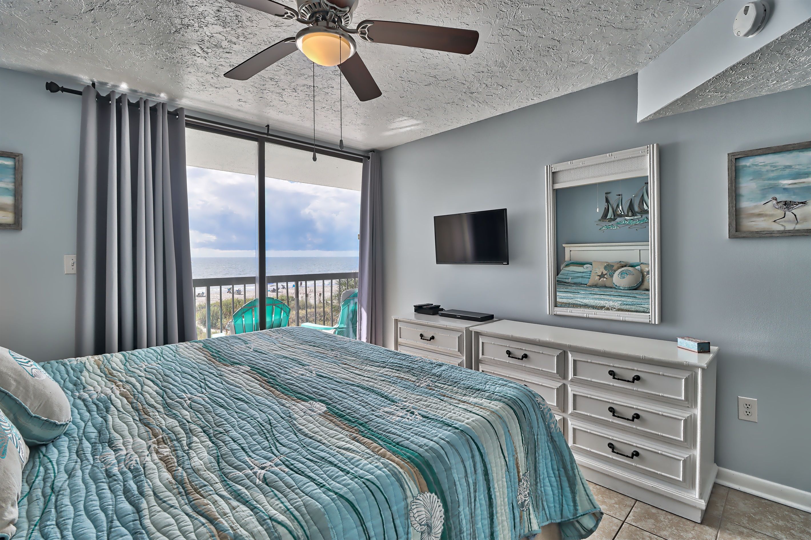 Een slaapkamer met een bed, een plafondventilator, een televisie, een dressoir en uitzicht op de oceaan.