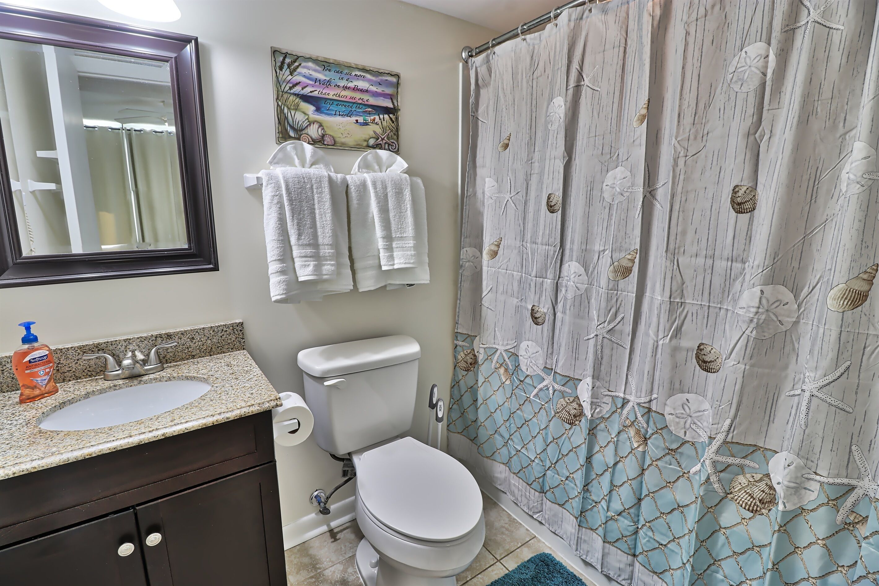 Un baño con lavamanos, inodoro y cortina de ducha con motivos playeros.