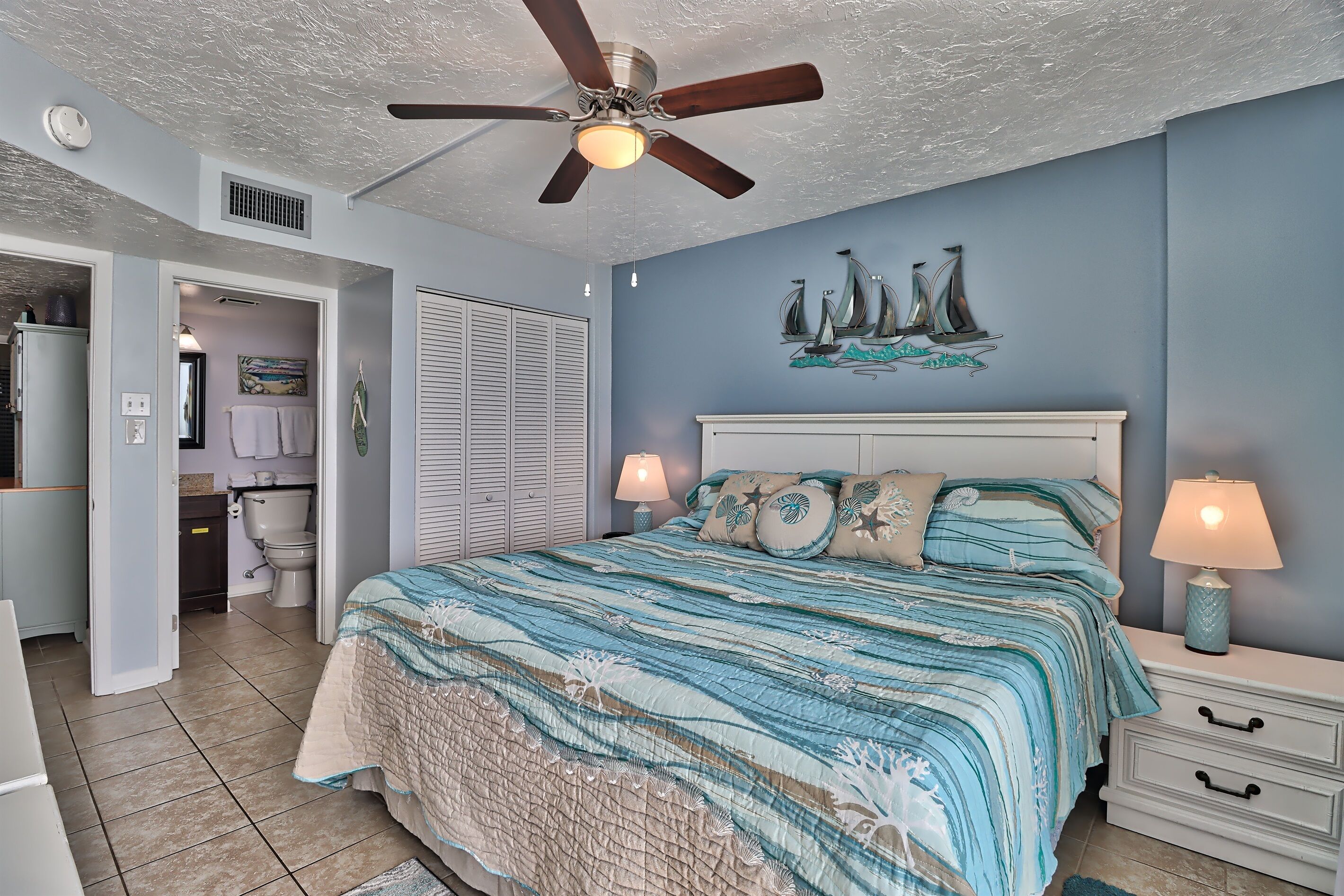 A bedroom with a bed, nightstands, a ceiling fan, and a wall-mounted artwork.