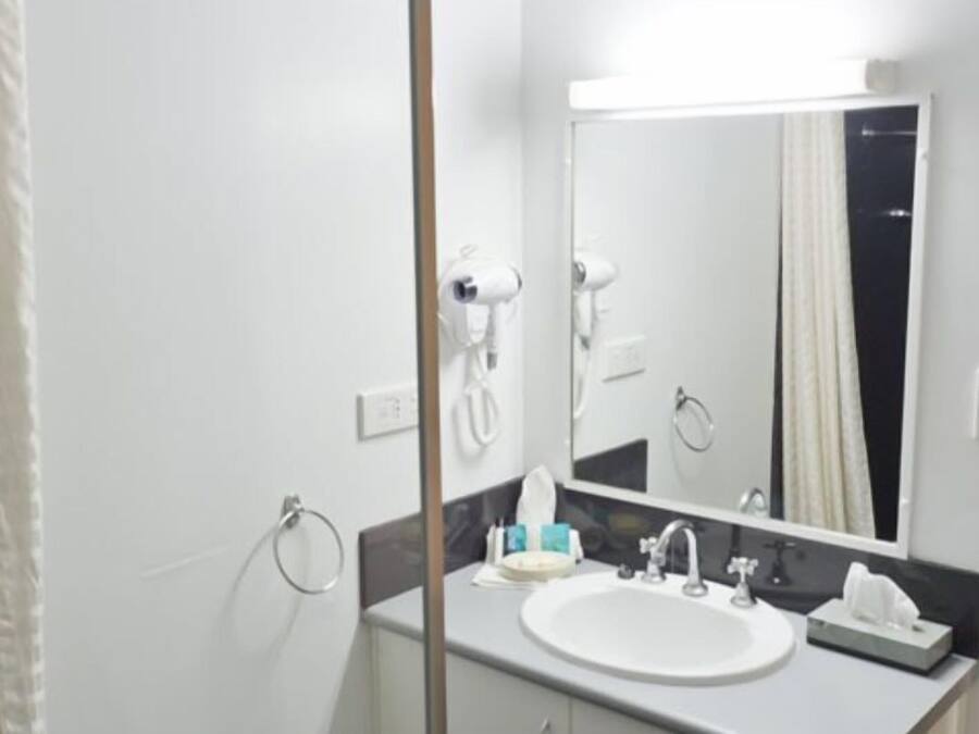 A bathroom with a white sink, a mirror, and a hairdryer mounted on the wall.
