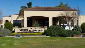 Un motel con un letrero que dice 'Motel de Grande', rodeado de jardines bien cuidados y un cielo azul despejado.