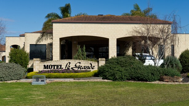 A motel with a sign reading "Motel de Grande," surrounded by well-maintained landscaping and a clear blue sky. - Motel Le Grande (Orana)