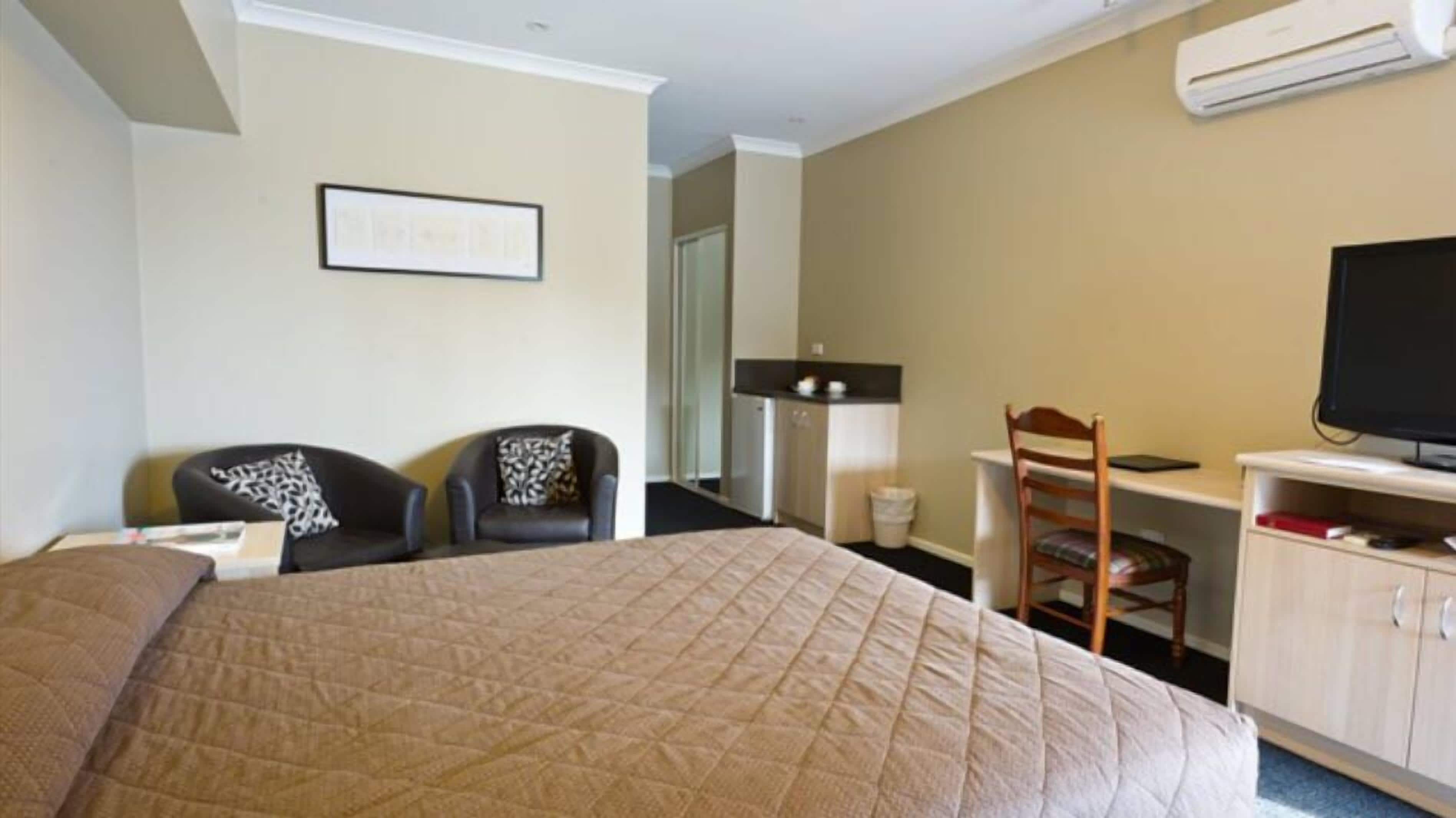 Una habitación de hotel con una cama grande, dos sillones, un escritorio con silla, televisión y una pequeña kitchenette.