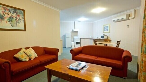 Un espacio habitable compacto con dos sofás rojos, una mesa de centro de madera, una zona de cocina con refrigerador, microondas y lavaplatos, y una mesa de comedor con sillas.