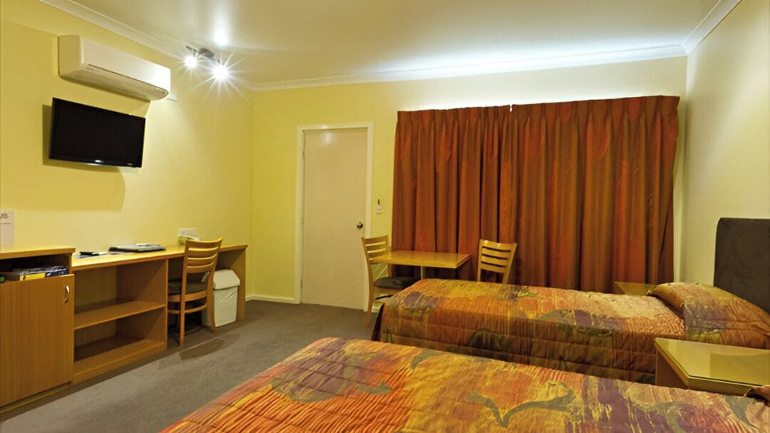 A hotel room with two beds, a desk, a chair, a television, and a wardrobe.