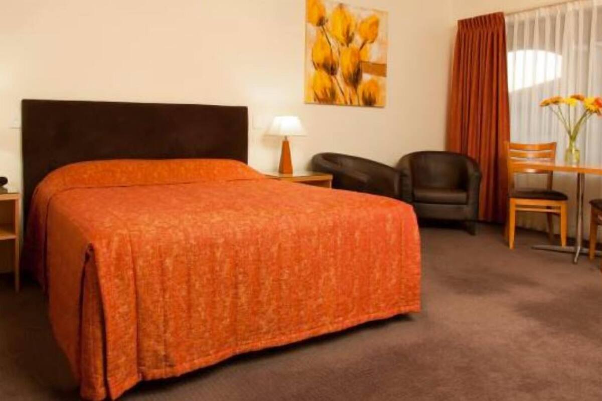 Une chambre d’hôtel avec un grand lit, un bureau avec une chaise, une petite table avec une chaise et un tableau au mur.