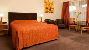 A hotel room with a large bed, a desk with a chair, a small table with a chair, and a painting on the wall.