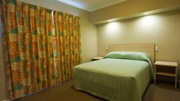 Een hotelkamer met een bed, nachtkastje en gordijn.