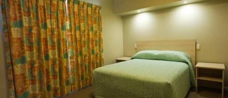 A hotel room with a bed, a nightstand, a bedside table, and a curtain.