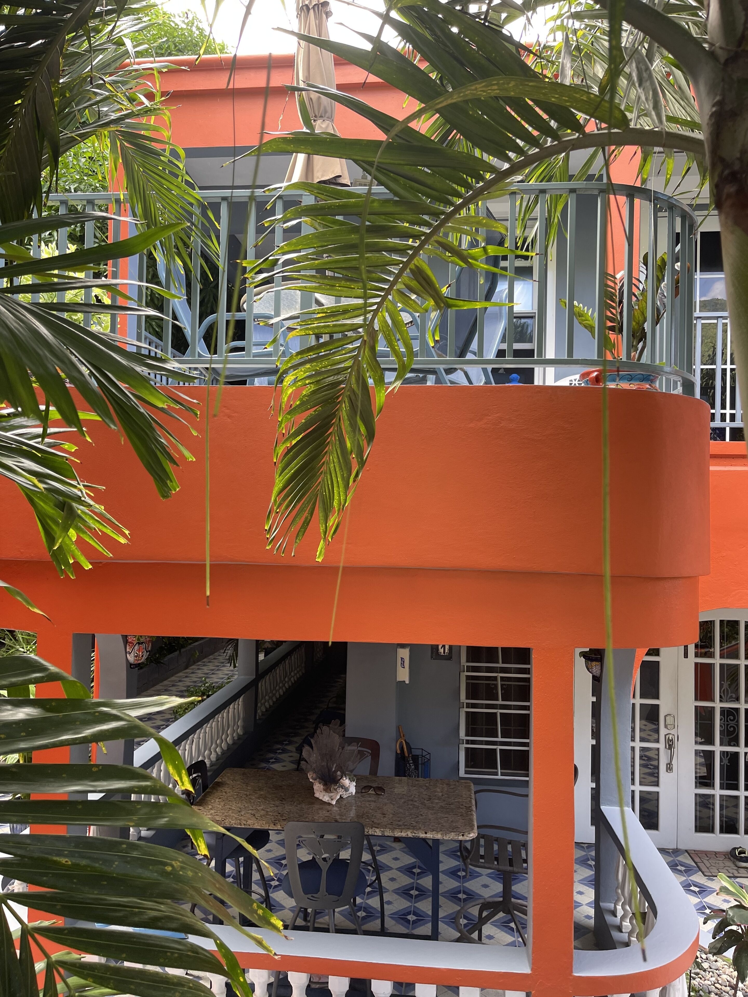 Un immeuble à plusieurs étages, à la façade orange, doté d’un balcon avec une balustrade et d’un espace repas comprenant des chaises et une table.