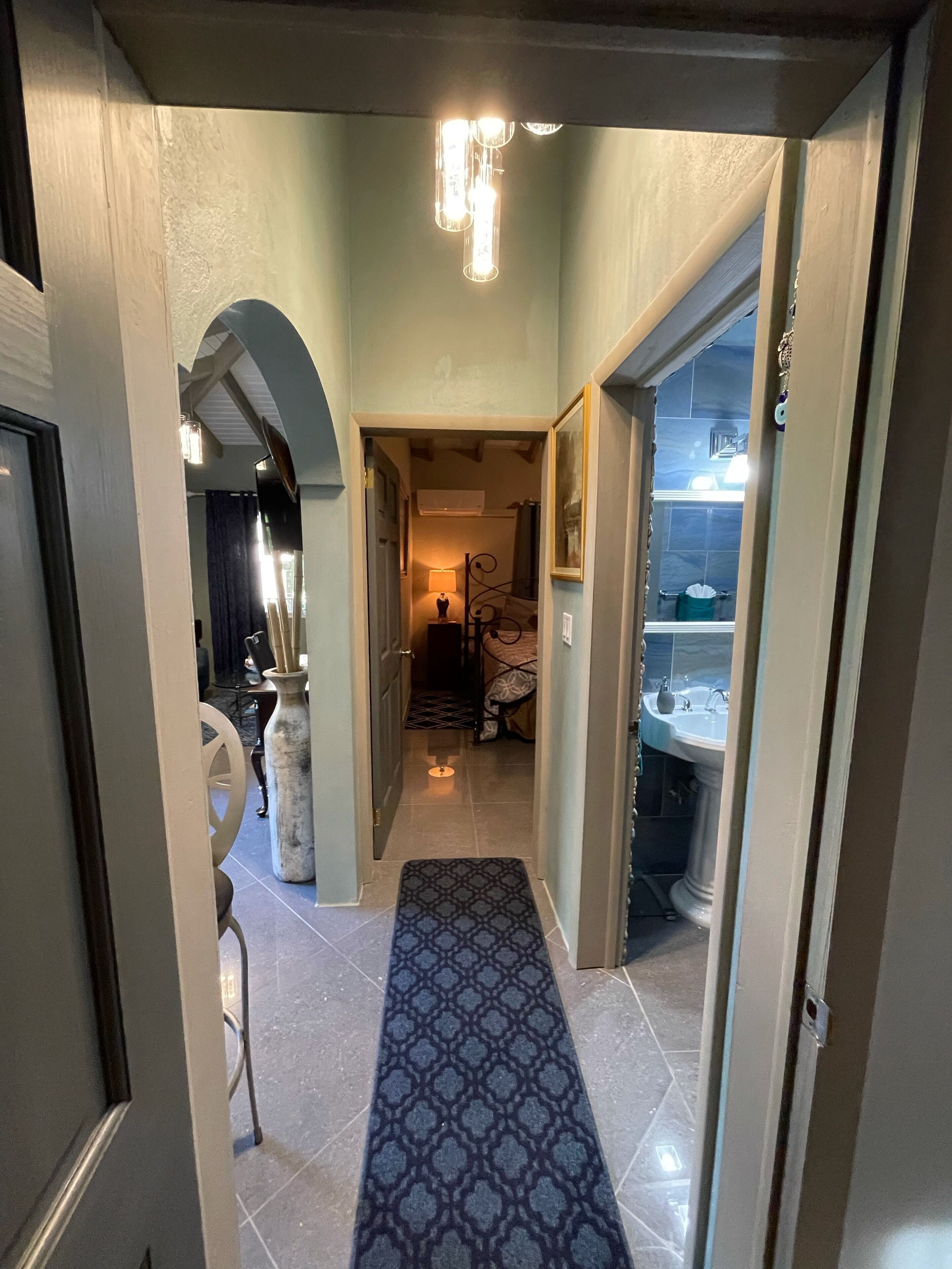 A hallway with a patterned carpet leading to a bathroom with a sink and mirror.