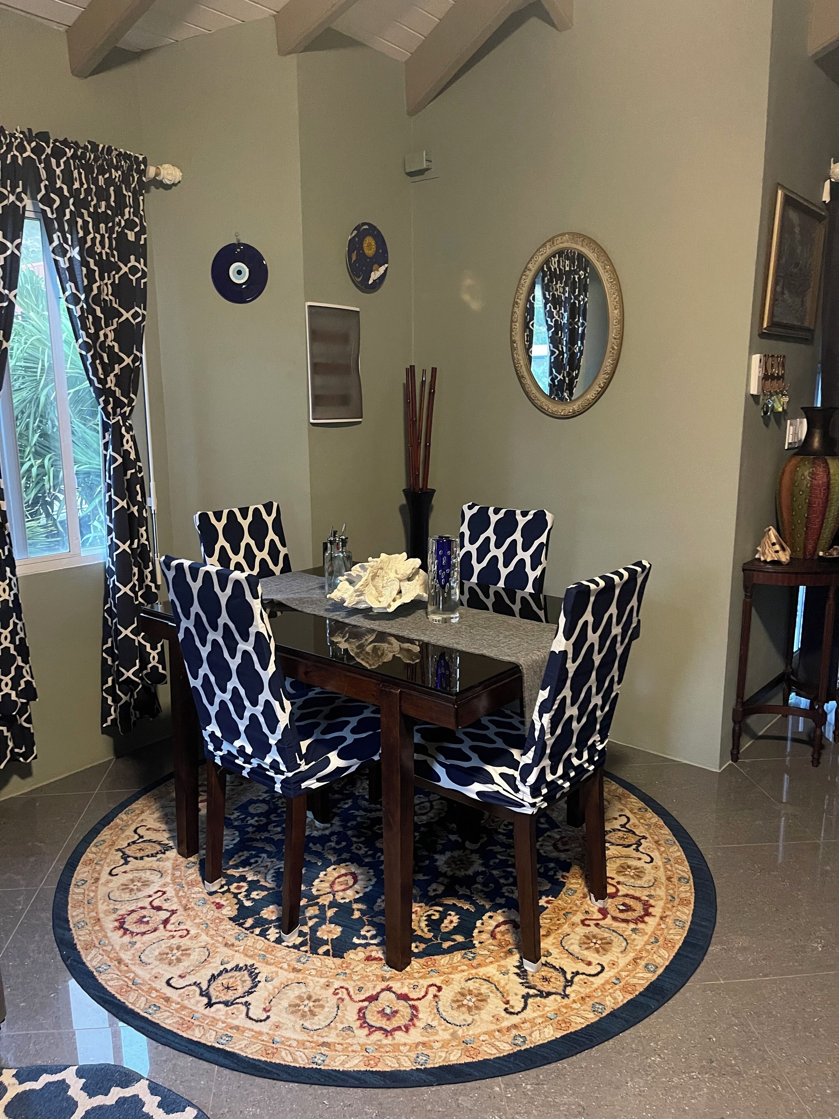 Un coin repas comprenant une table ronde, quatre chaises à motifs noir et blanc, un miroir décoratif et un tapis à motifs.