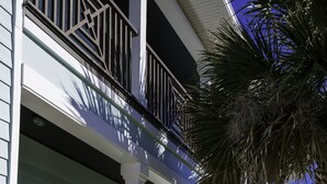 Une maison à deux étages avec un porche couvert, des balustrades en bois et un palmier au premier plan.