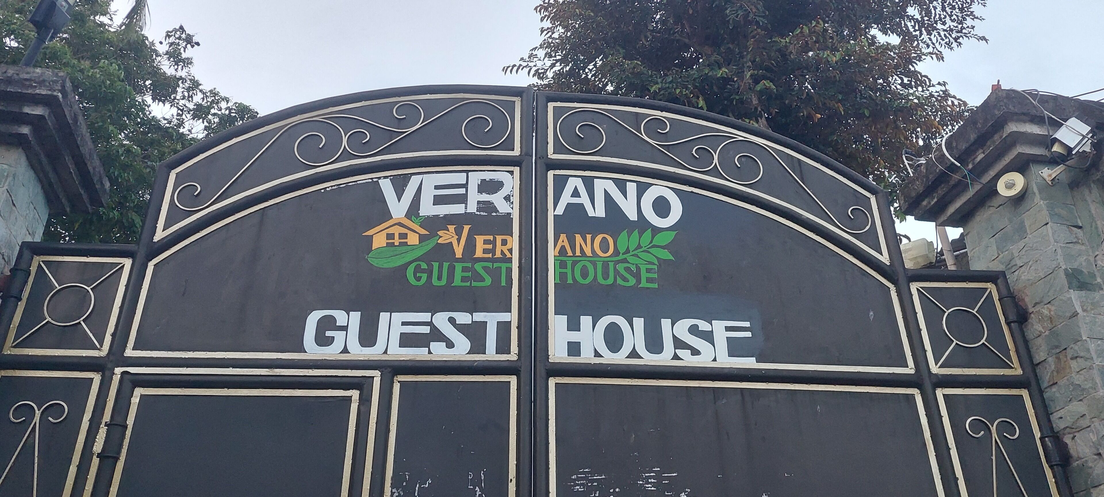 Une porte noire ornée des mots « VERANO GUEST HOUSE » et de motifs décoratifs en spirale.