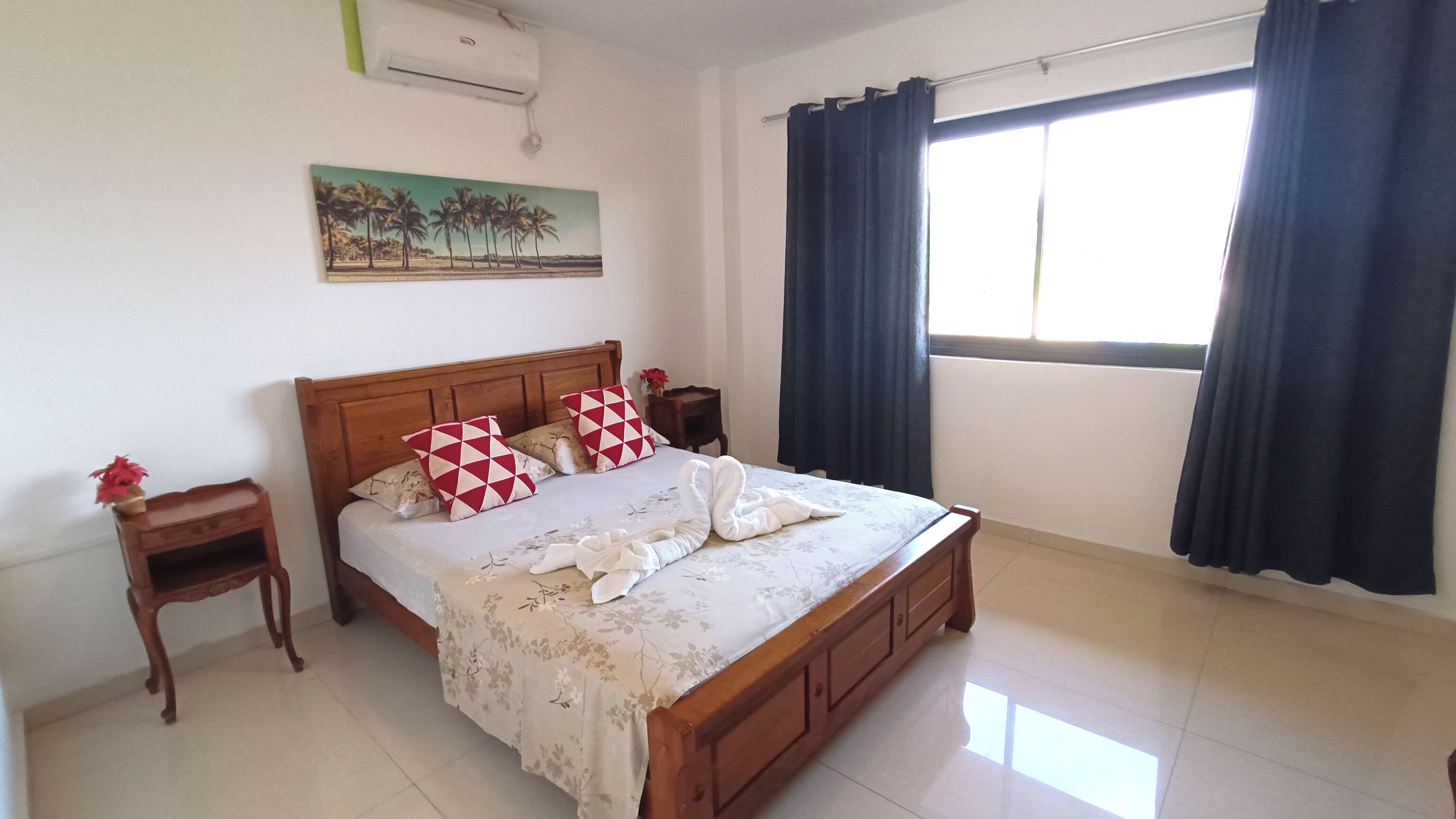 A bedroom with a wooden bed, two nightstands, a painting on the wall, and a window with curtains.