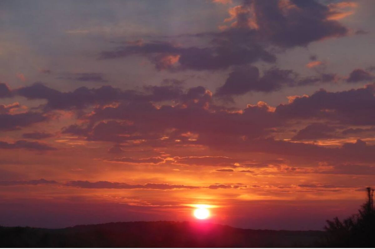 Ein Sonnenuntergang über einer hügeligen Landschaft mit blauem Himmel und vereinzelten Wolken.