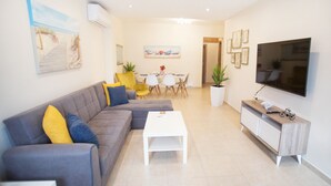 Una sala moderna con un sofá gris, una mesa de centro blanca y un televisor sobre un mueble de madera.