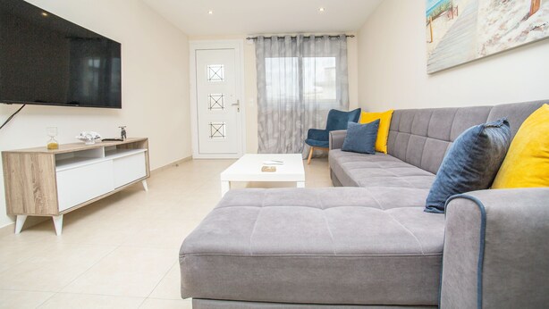 Una sala de estar moderna con un sofá gris, una mesa de centro blanca y un televisor montado en la pared.