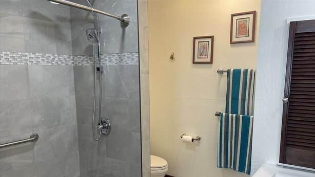 Et badeværelse med glasvæg omkring brusebad, toilet og håndvask.