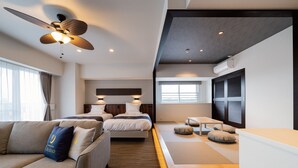 Una camera d'hotel moderna con un divano, due letti, una ventola a soffitto e un piccolo tavolo.