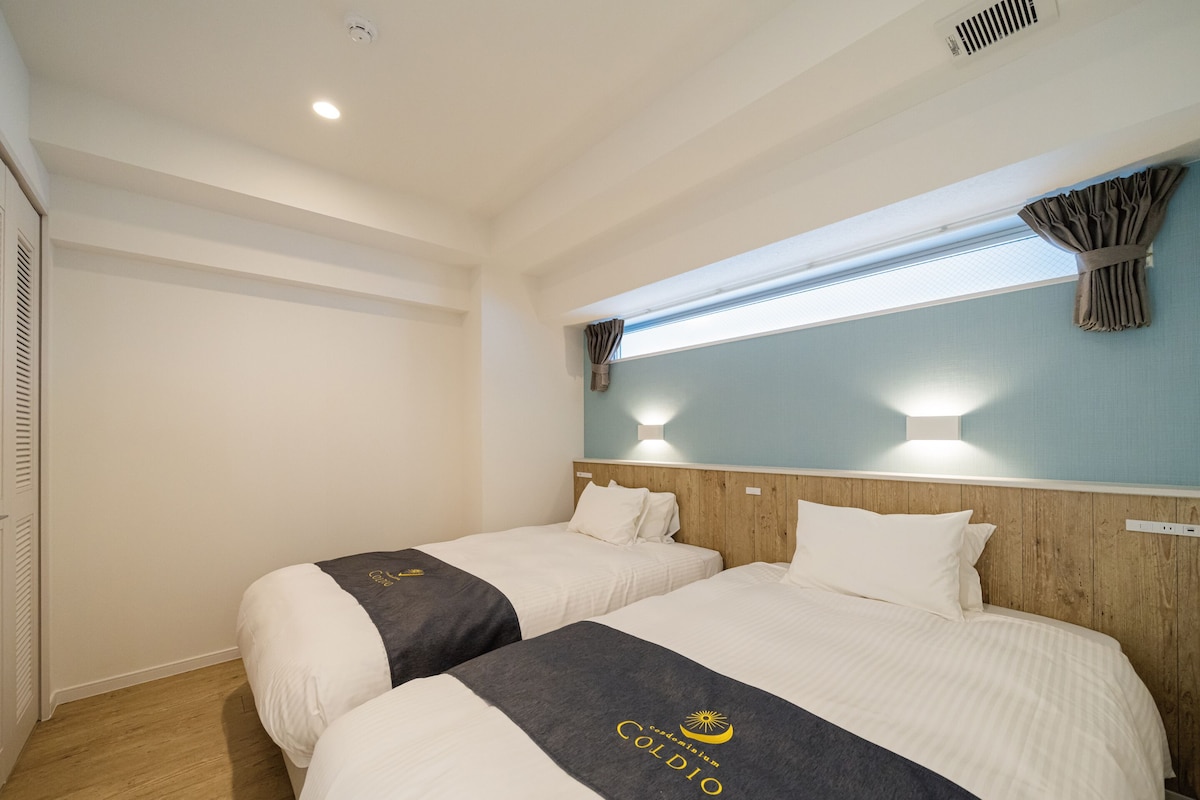 Habitación de hotel con dos camas, cabecero de madera, ventana con cortinas y un respiradero en el techo.
