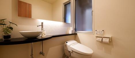 Un baño pequeño y funcional con lavamanos blanco, inodoro y ducha, además de un ventanal.