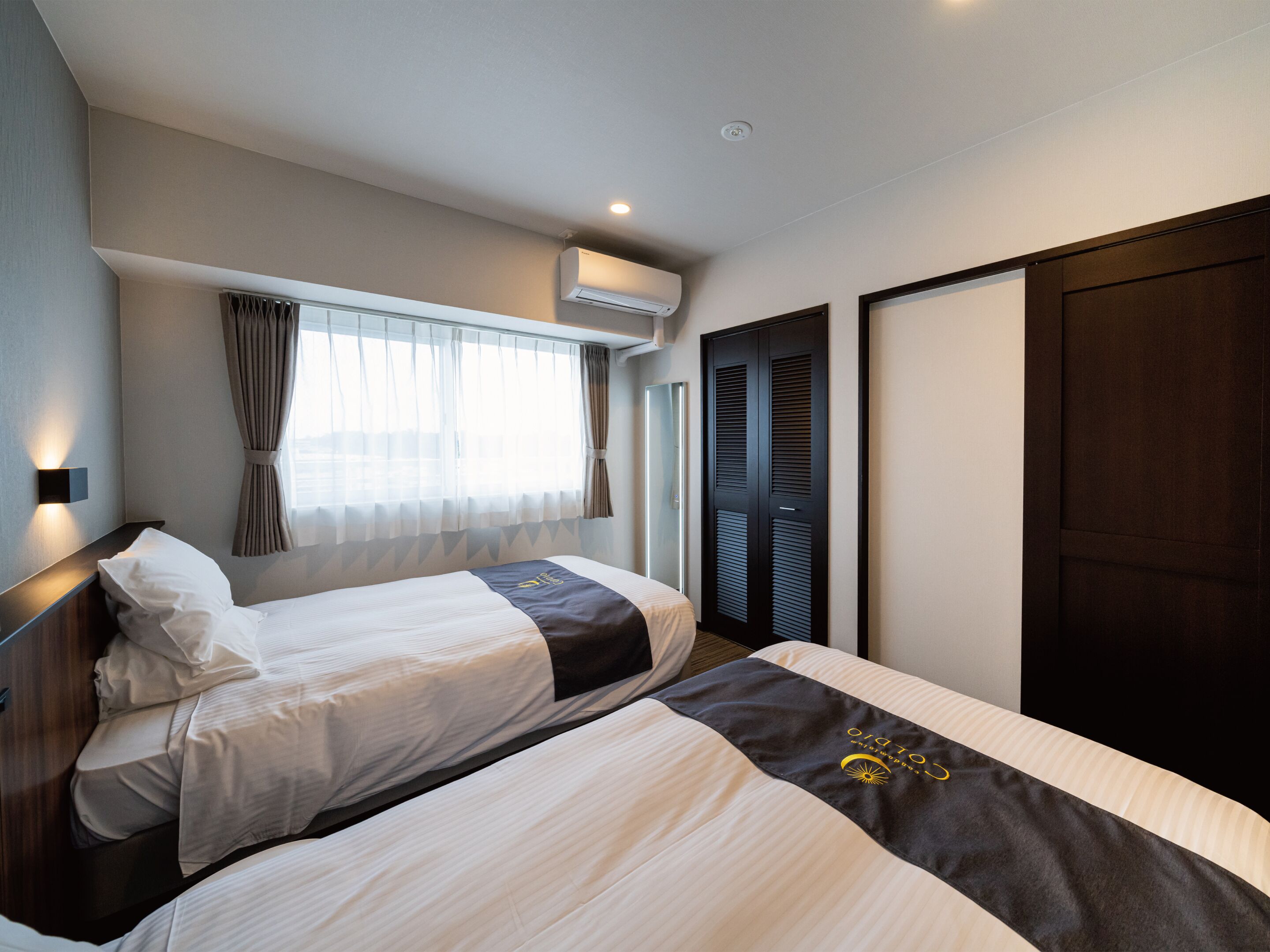 Une chambre d’hôtel avec deux lits, une fenêtre avec des rideaux, un appareil de climatisation et une armoire.