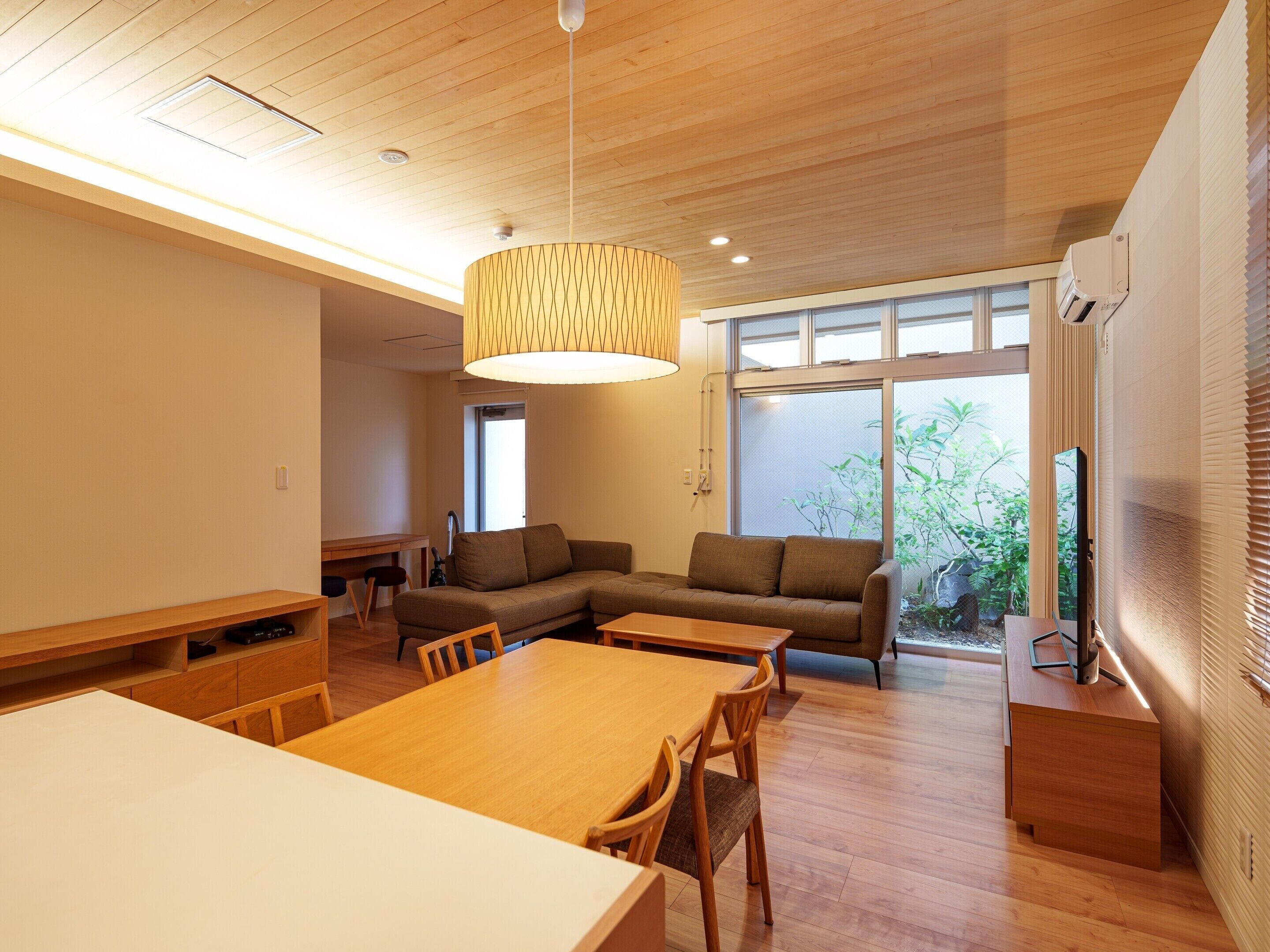 Una sala moderna con una mesa de comedor de madera, sofá y un ventanal con vistas a zonas verdes.