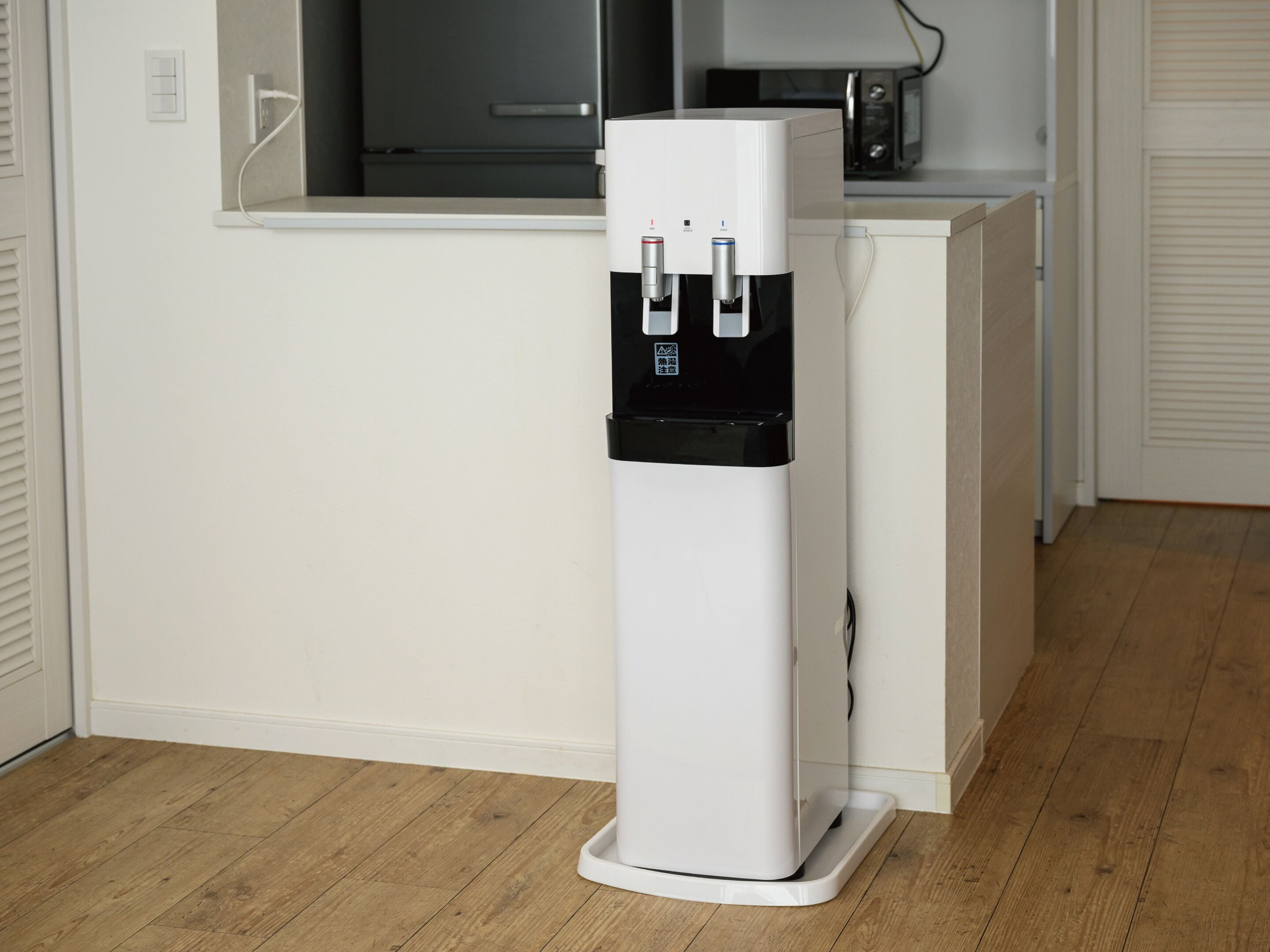 A water dispenser in a modern kitchen with white cabinets and a wooden floor.