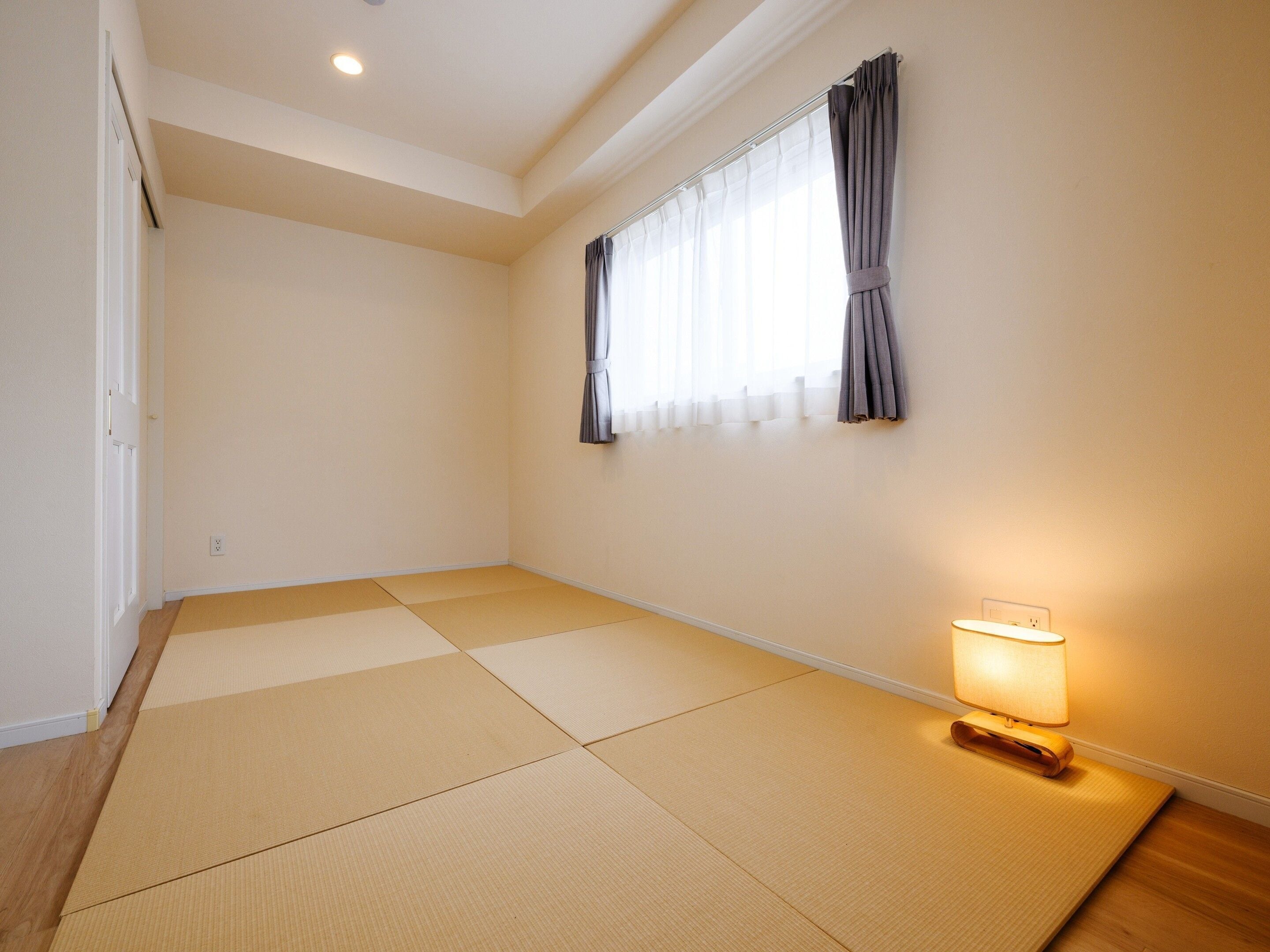 Una habitación con suelo de esteras de tatami, una ventana con cortinas y una lámpara de noche.