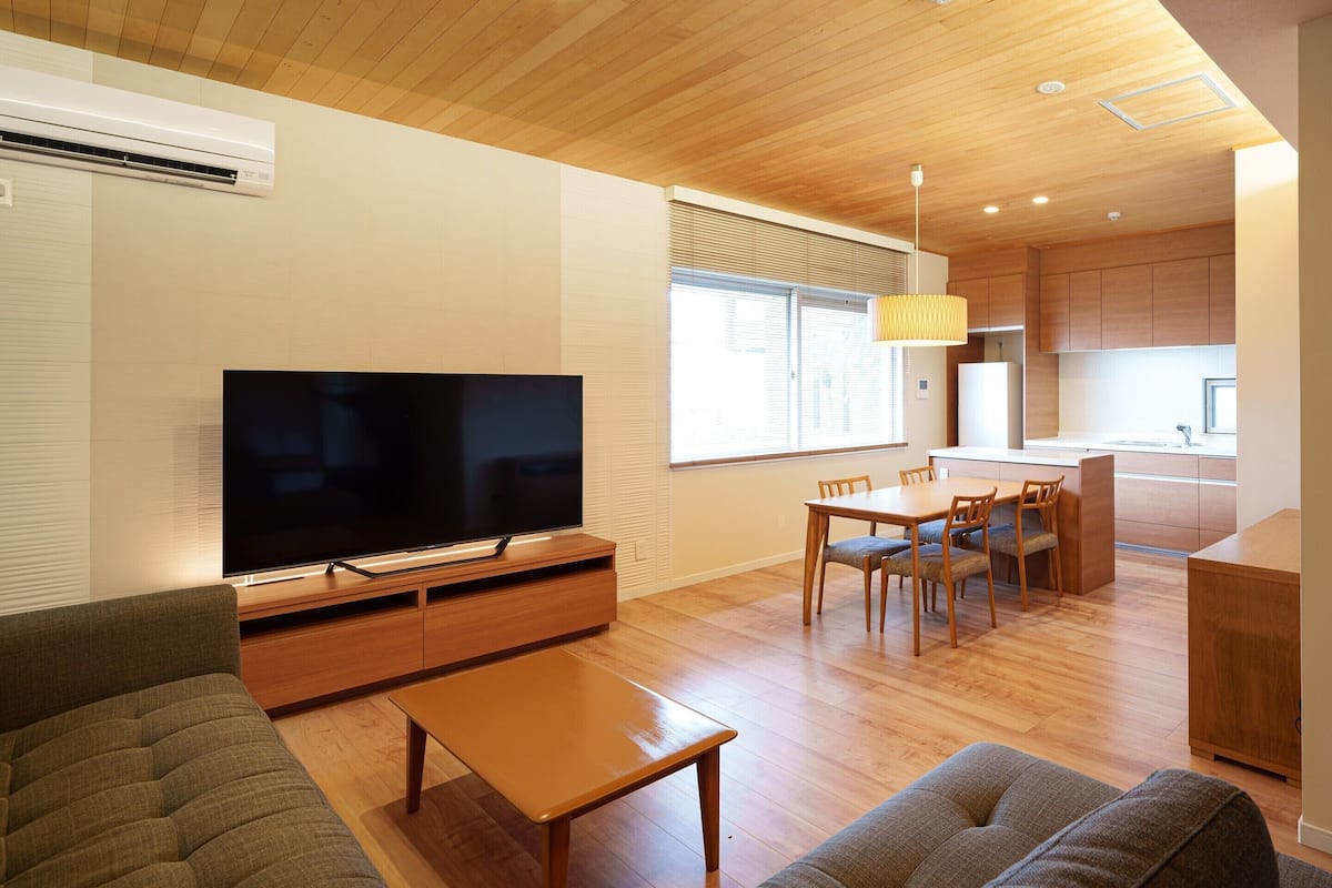 A modern living room with a flat-screen TV, wooden furniture, and a dining area with a table and chairs.