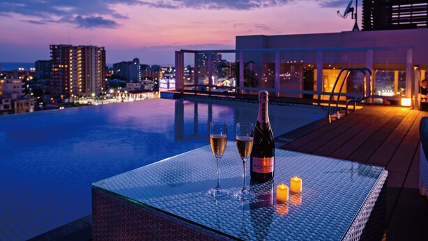 Area piscina sul tetto con un tavolo apparecchiato per due, una bottiglia di champagne e candele.