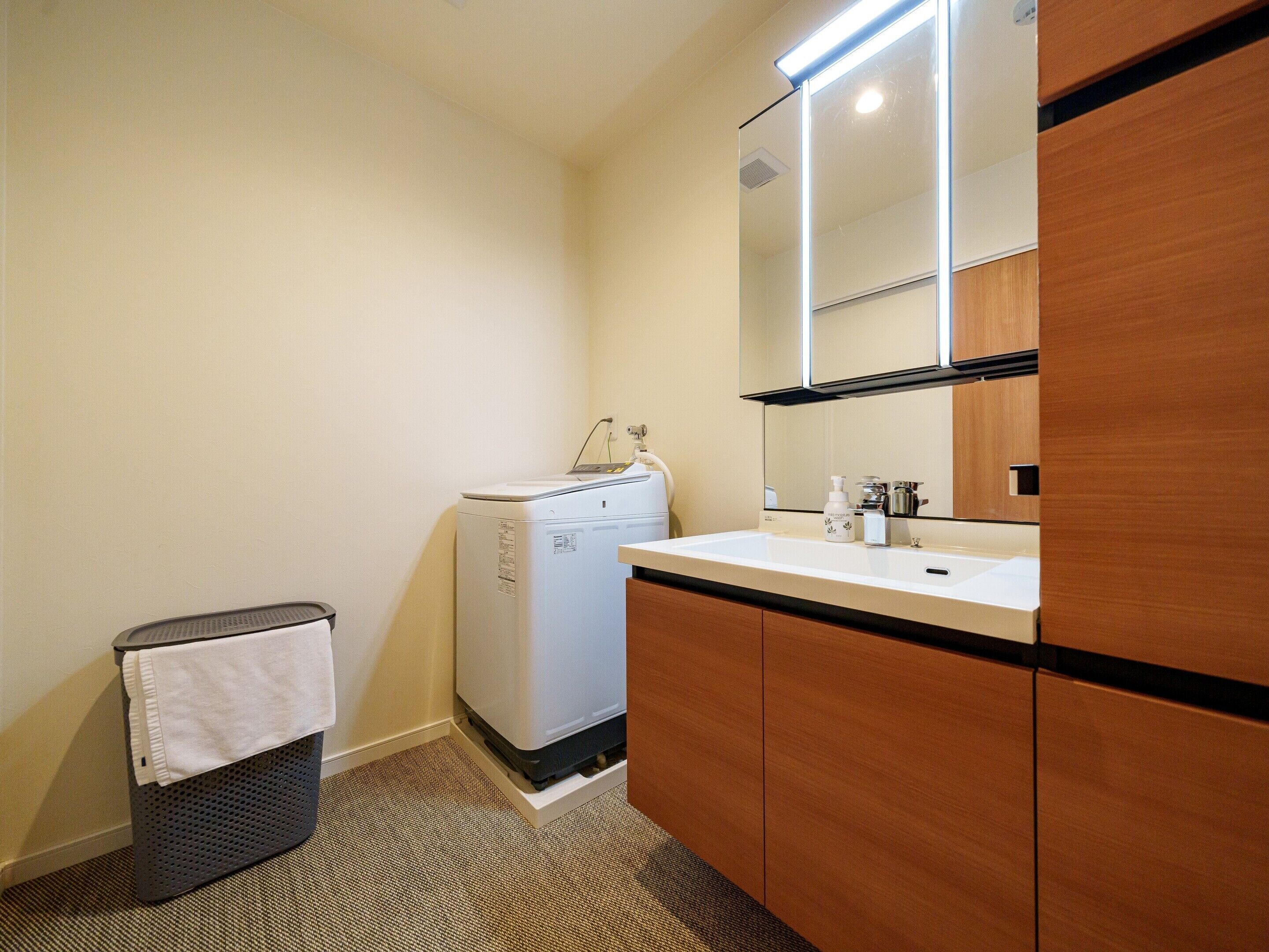 A small, clean bathroom with a washing machine, a sink, and a mirror.