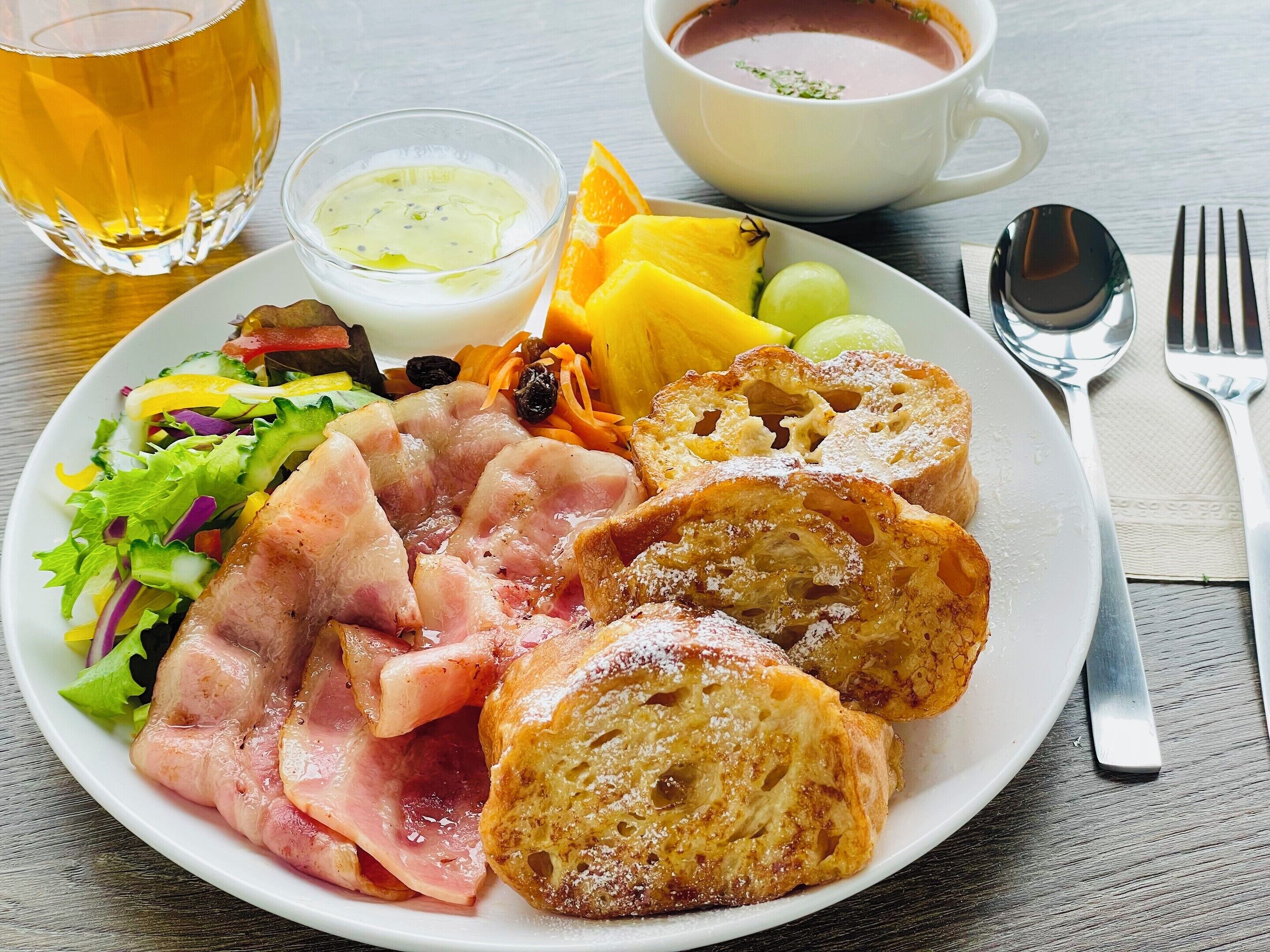 A plate with ham, bread, a salad, and a cup of soup.