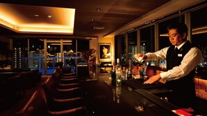 Zona bar con un barista che prepara un cocktail, un bancone e un'area con sedute.