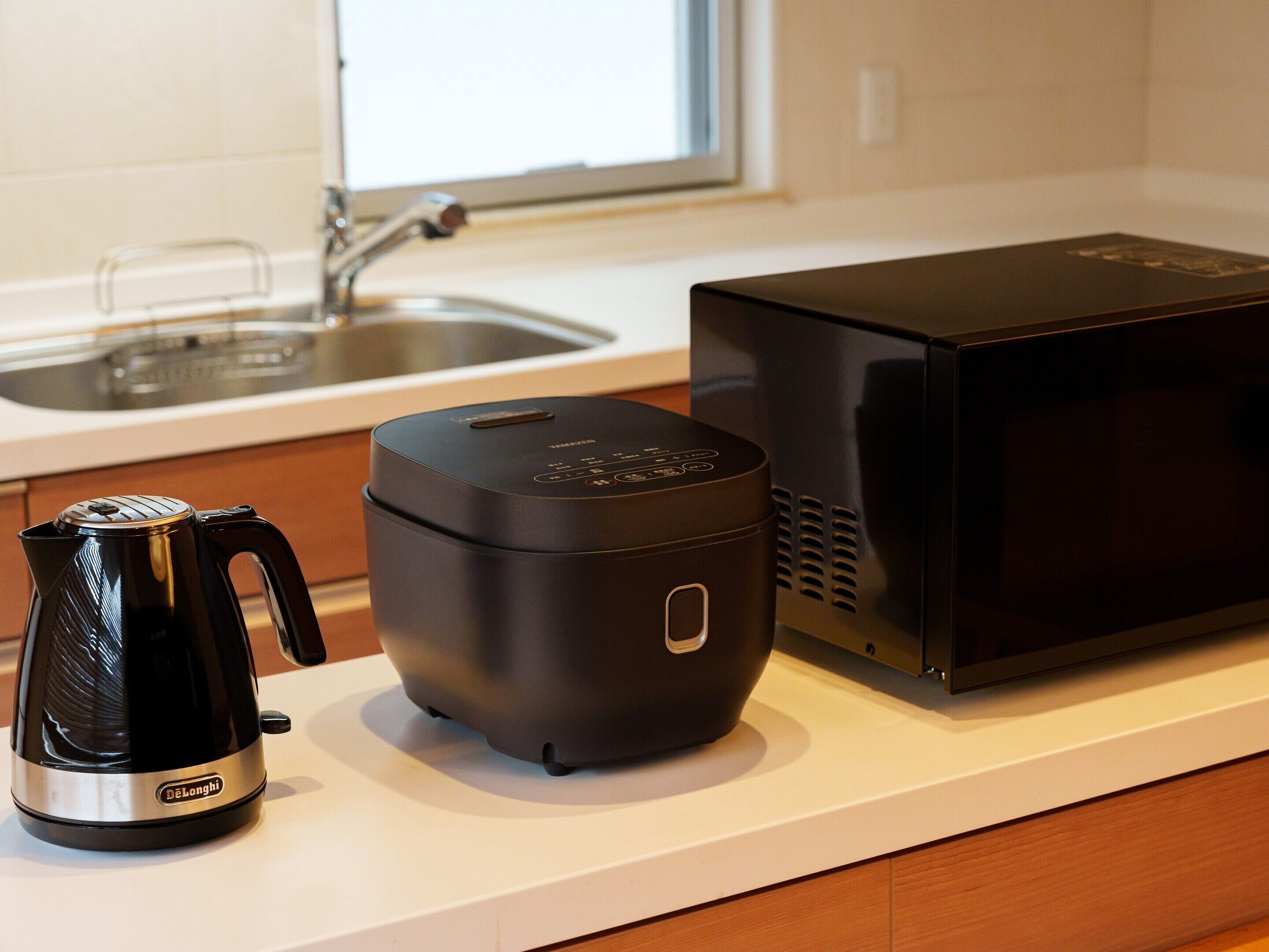 A kitchen with a black coffee maker, a black electric kettle, and a black microwave on the counter.