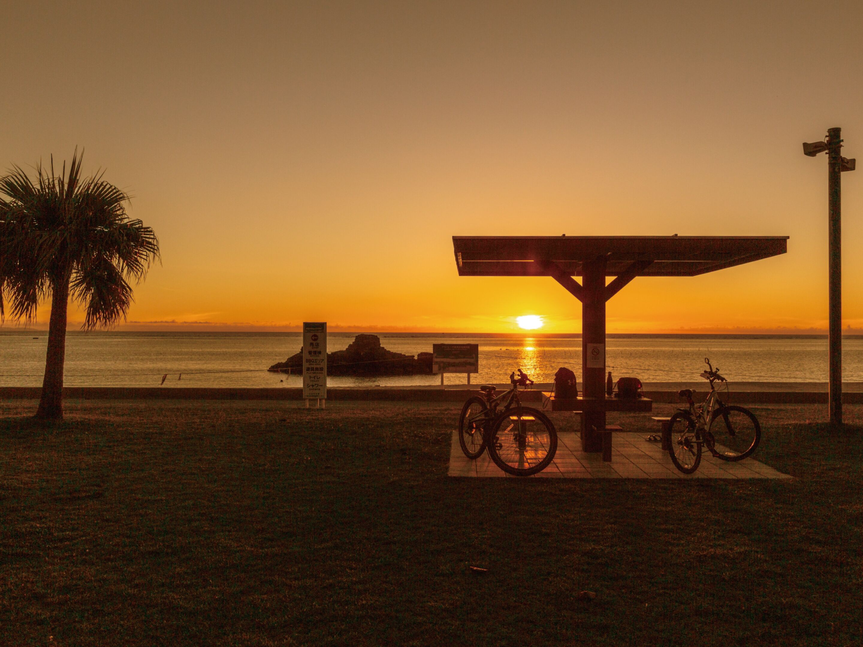 A sunset view with a beach, a covered seating area, and bicycles.
