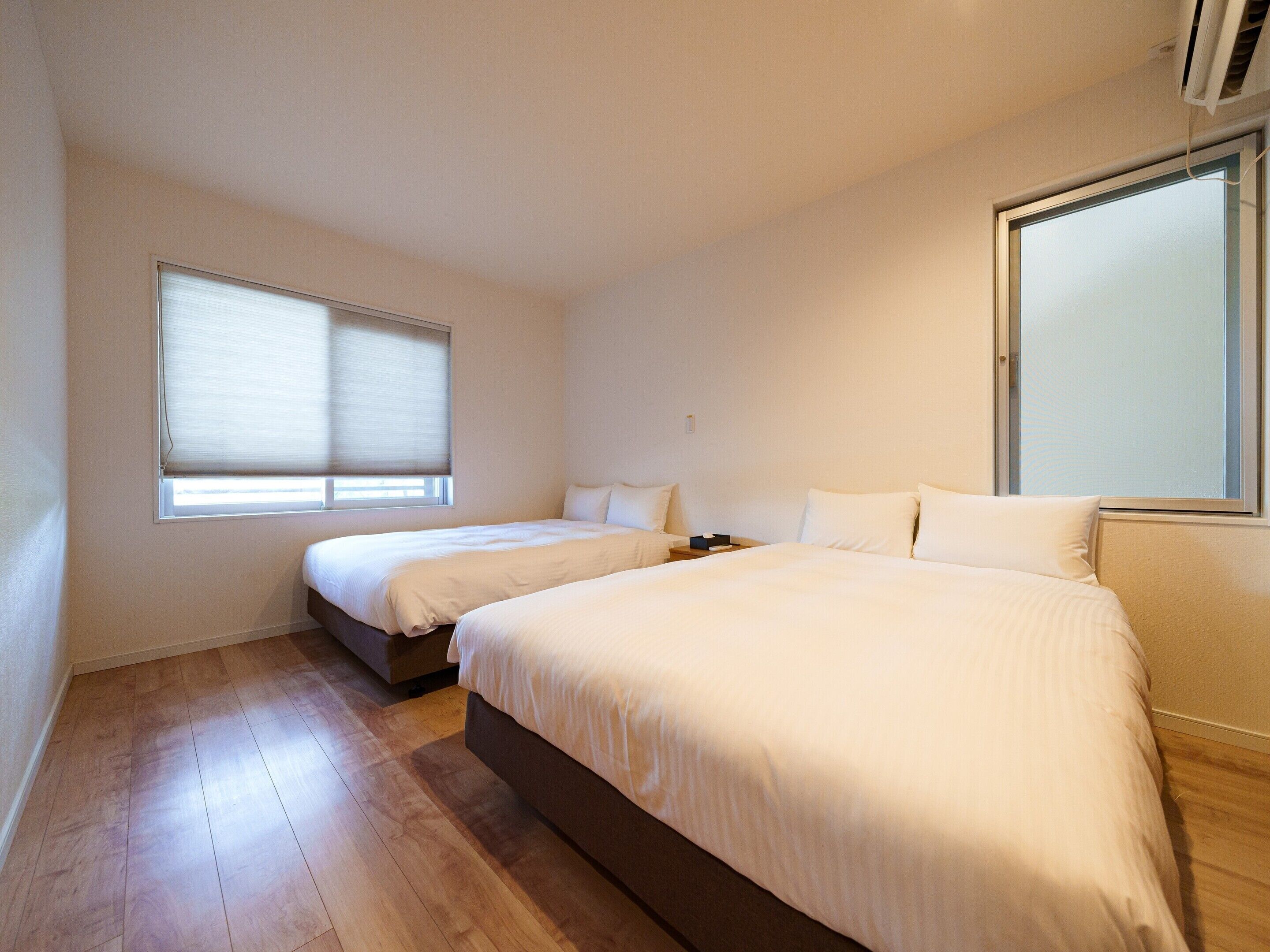 Una habitación de hotel con dos camas, un ventanal grande y suelo de madera.