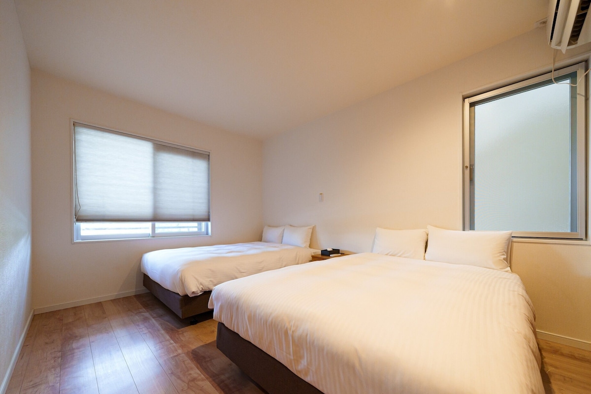 Una habitación de hotel con dos camas, un ventanal grande y suelo de madera.