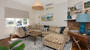 A cozy living room with a patterned sofa, a woven pendant light, and a brick accent wall. - Original 1950's beach cottage (Mollymook)