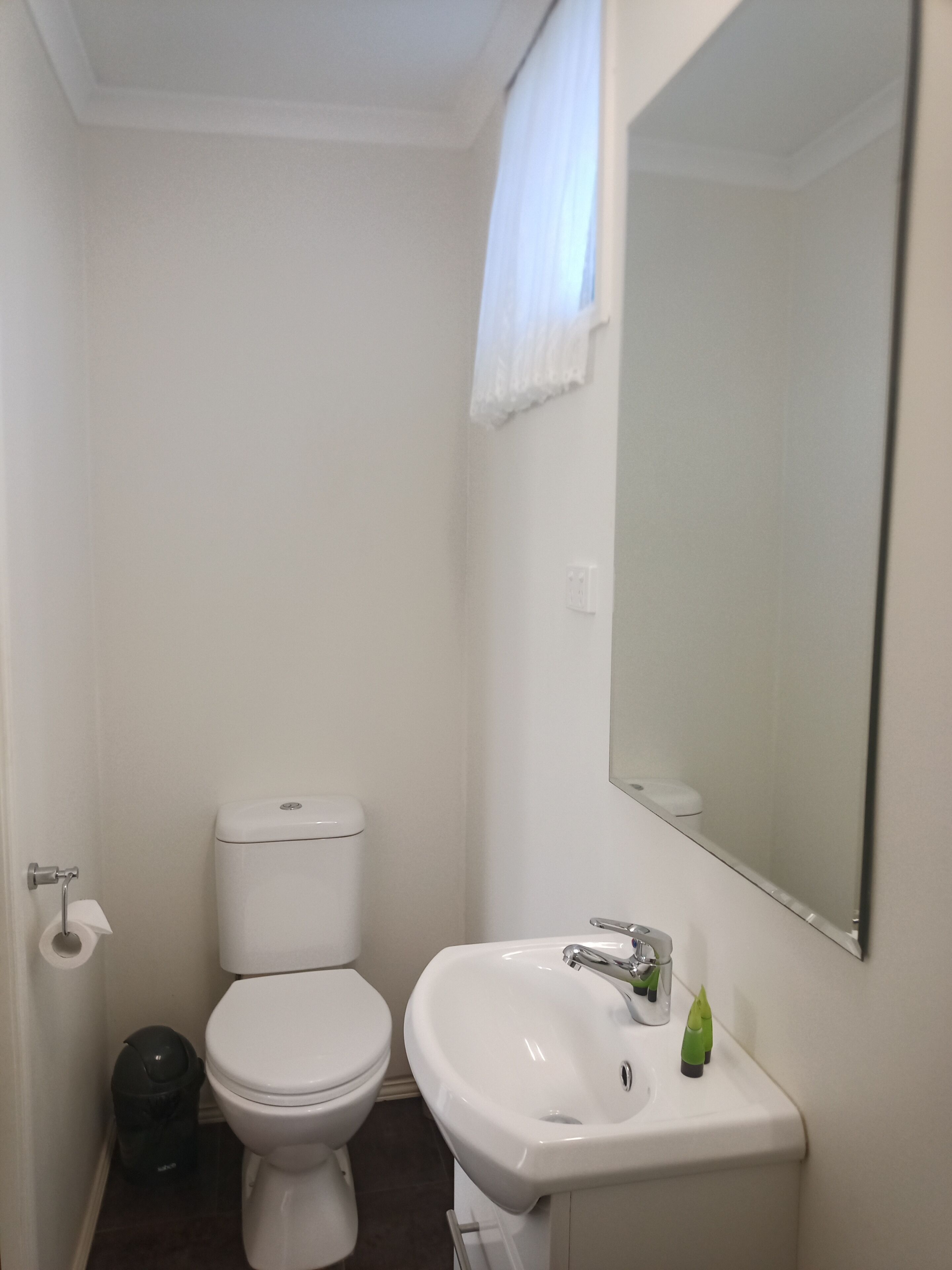 A small, clean bathroom with a toilet, sink, and mirror.
