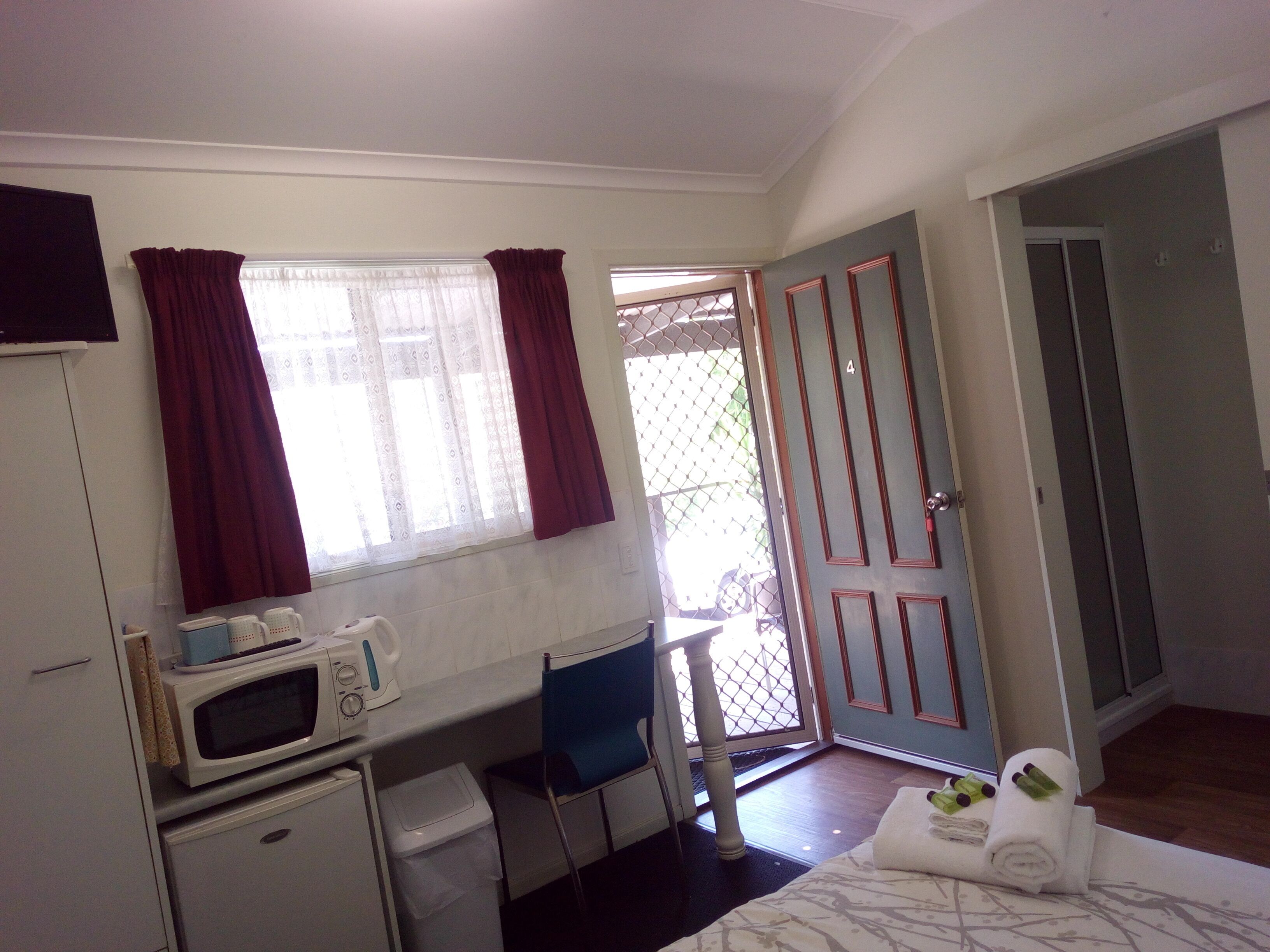 A small room with a bed, a desk with a microwave, a chair, and a door leading to a balcony.