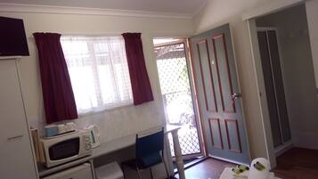 A small room with a bed, a desk with a microwave, a chair, and a door leading to a balcony.